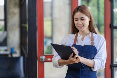 Asian woman in apron holding restaurant menu in front of door with open sign, small restaurant concept
