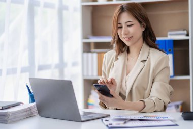 Asian businesswoman working with financial documents, discussing with clients with smartphone and laptop computer on table, analysis plan, financial report. Business plan. Investment finance concept.