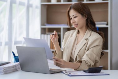 Asian businesswoman working with financial documents and laptop Inside office worker calculating financial indicators smiling and happy with success and results of business success