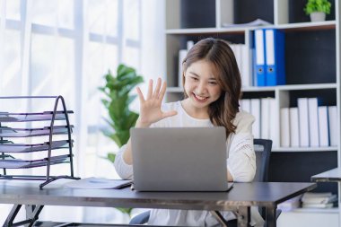 Asian young accountant meeting online video call on laptop waving greetings to colleague