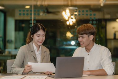 Two asian male and female employees looking at documents, financial graphs and laptop screens using video conferencing with colleagues in field. financial accounting concept