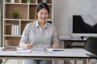Young black-haired asian female worker working in office with financial documents and laptop calculating company annual budget accounting.