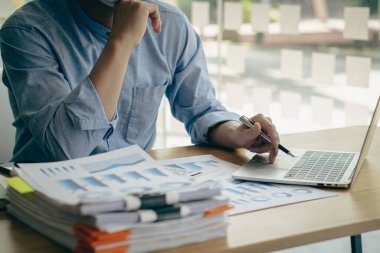 Bürokraside çalışan işadamı dizinlere dizilmiş dizüstü bilgisayarlar ve dokümanlar ile ofis hesap raporunda bilgi arıyor. Masadaki tamamlanmamış evrak işlerini hallediyor..