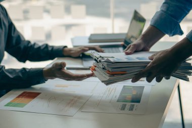 Bürokraside çalışan işadamı dizinlere dizilmiş dizüstü bilgisayarlar ve dokümanlar ile ofis hesap raporunda bilgi arıyor. Masadaki tamamlanmamış evrak işlerini hallediyor..