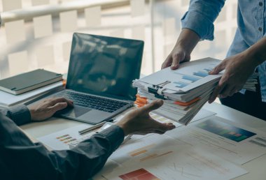 Bürokraside çalışan işadamı dizinlere dizilmiş dizüstü bilgisayarlar ve dokümanlar ile ofis hesap raporunda bilgi arıyor. Masadaki tamamlanmamış evrak işlerini hallediyor..