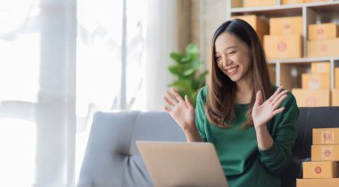 Küçük bir iş kurun, genç Asyalı bir kadın çevrimiçi alışveriş yaparak kutuları paketliyor ve dijital dizüstü bilgisayardan müşterilere teslim edilecek ürünleri kontrol ediyor..
