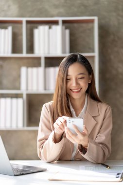 Genç Asyalı iş kadını hesaplama yapmak için hesap makinesine basmaya başlayacak dizüstü bilgisayarla kontrol etmesi ya da raporların doğruluğunu analiz ederek şirket finansmanını hazırlamak için grafikli verileri gösterecek.