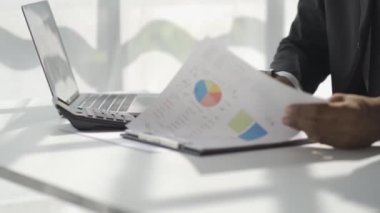 Afrikalı adam masasında oturuyor ve belgeleri inceliyor. Aylık raporların analitik 4K 'da çalıştığını gösteren raporları ve finansal detayları okuyor.