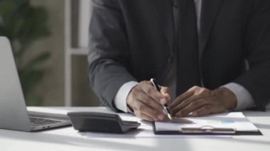 Afrikalı adam masasında oturuyor ve belgeleri inceliyor. Aylık raporların analitik 4K 'da çalıştığını gösteren raporları ve finansal detayları okuyor.