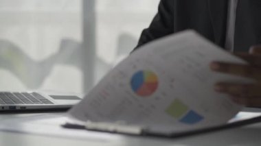 Afrikalı adam masasında oturuyor ve belgeleri inceliyor. Aylık raporların analitik 4K 'da çalıştığını gösteren raporları ve finansal detayları okuyor.