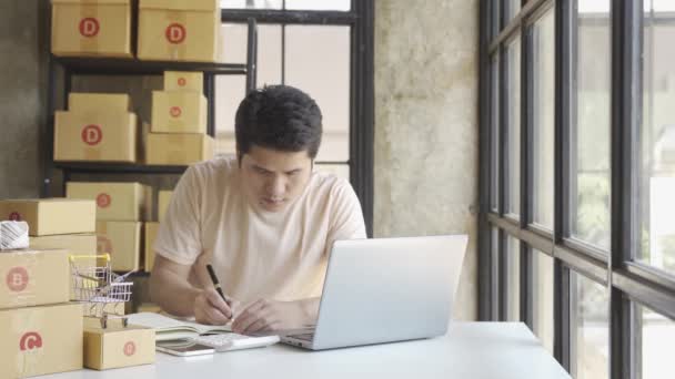 Tişörtlü Genç Asyalı Işadamı Ofisinde Dizüstü Bilgisayarla Çalışıyor Siparişleri Alıyor — Stok video