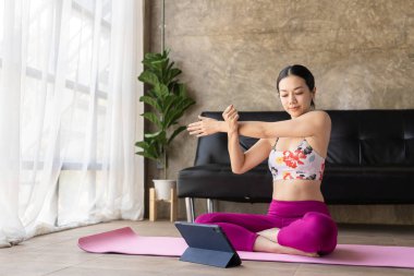 Sağlıklı Asyalı kadın tablet üzerinde egzersiz videosu seyrediyor. Evde yoga yapıyor. Evde sağlıklı ve güçlü kalmak için tablet üzerinde pratik yapıyor.