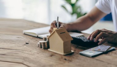 House of piles of coins in front notebook and pen Young man writing by hand. Prepare a plan. Saving coins to buy a house as real estate.