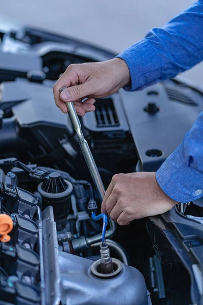 Man inspecting and fixing his car using wrench while working on broken engine on road Car service and maintenance checks vertical image