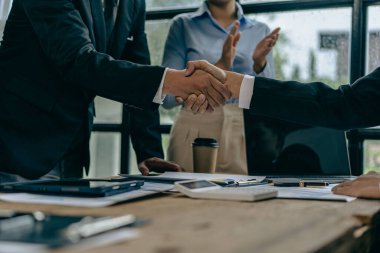 Two businessmen shaking hands making a money deal for handshake discussing successful financial business in conference room