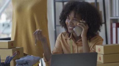 Genç siyahi kadın internetten kıyafet satıyor akıllı telefonlardan alışveriş işi konseptiyle sipariş alıyor. Kadın girişimci evden çalışıyor.