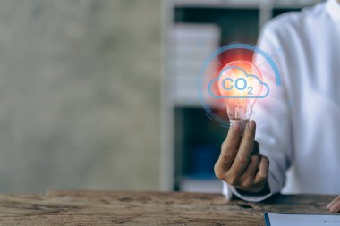 Businessman hand holding light bulb with natural energy icons, financial documents and tools for inspiration and creativity. Science innovation technology and communication network connection