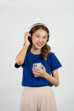 Beautiful young woman holding her mobile phone and wearing headphones and listening to music with smile on her face, white background. concept of online entertainment with music streaming