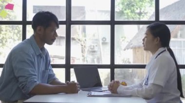 Asian young female nurse doctor holding patient's hand giving advice and encouragement, showing compassion, supporting diagnosis at medical health care consultation.
