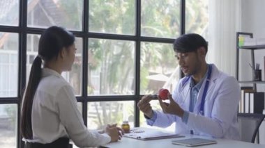 Friendly doctor or Asian male helping discuss medicine and heart disease with medical tests at clinic desk. A young woman with severe stress visits a doctor at the hospital.