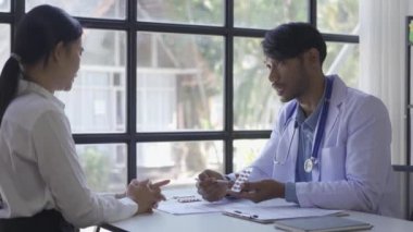 Friendly doctor or Asian male helping discuss medicine and heart disease with medical tests at clinic desk. A young woman with severe stress visits a doctor at the hospital.