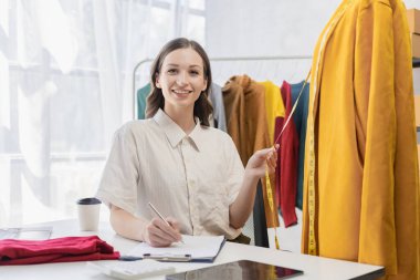 A beautiful blogger shows off her clothes in front of a smartphone camera while recording videos, vlogs and live streams at her store, online clothing sales concept on social media.