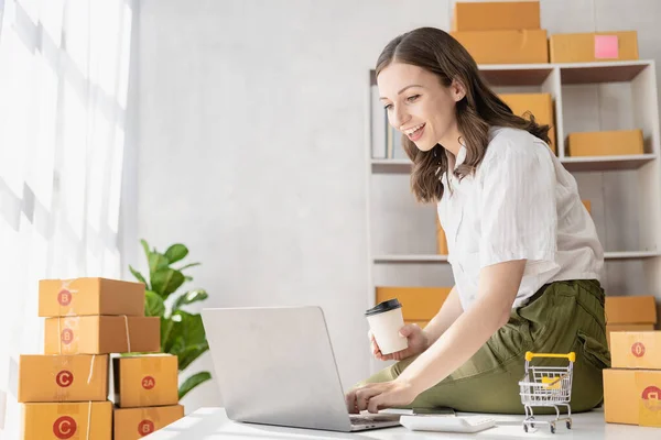 young woman starting an independent business Online shopping working on laptop computer with package box at table at home - SME business ideas online sales and delivery.