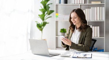 Confident businesswoman holding a smartphone work with financial statistics Diagram presentation on laptop screen female accountant analyzing data in the office