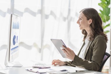 Confident smiling businesswoman using tablet working on financial statistics presentation with graph document, female accountant analyzing data in office
