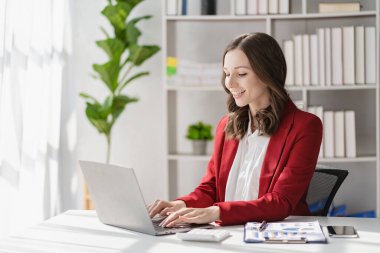 American businesswoman smiling confidently using laptop computer working on financial statistics presentation with graph document Female accountant analyzing data in office looking at camera