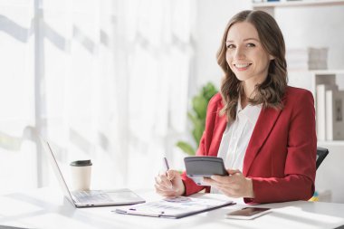 American businesswoman smiling confidently using laptop computer working on financial statistics presentation with graph document Female accountant analyzing data in office looking at camera