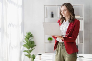 American businesswoman smiling confidently using laptop computer working on financial statistics presentation with graph document Female accountant analyzing data in office looking at camera
