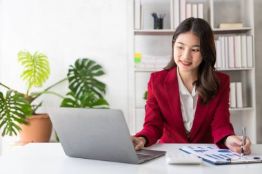 Asian businesswoman or accountant using calculator and laptop computer with graphs, analytical business reports and charts in workplace monthly accounting finance concept