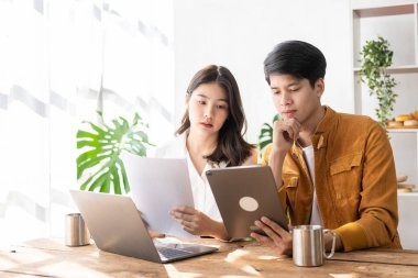 Two young Asian businessmen and a young woman use tablets to work together on business plans in the office. Businessman working on concept presentation, startup project, analyzing, planning.
