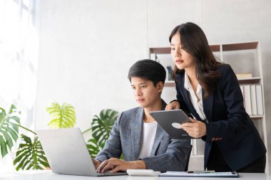 Two young Asian businessmen and a young woman use tablets to work together on business plans in the office. Businessman working on concept presentation, startup project, analyzing, planning.