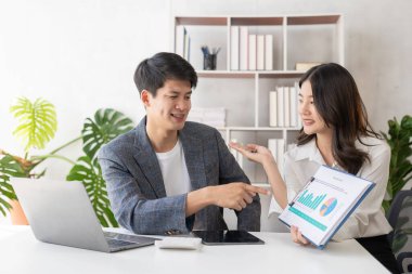 Cheerful young Asian couple working together in cozy living room at home. Couple working at home with laptop, financial accounting concept, pie in house