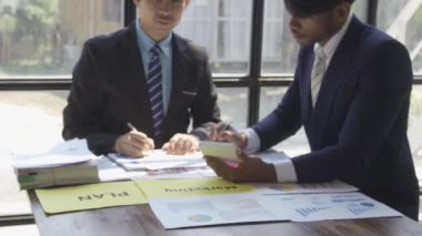 Two businessmen in suits discussing project on paper with graphs and charts. Pointing to Financial Documents in Dark Office 4K
