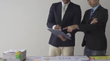 Two businessmen in suits discussing project on paper with graphs and charts. Pointing to Financial Documents in Dark Office 4K