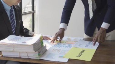 Two businessmen in suits discussing project on paper with graphs and charts. Pointing to Financial Documents in Dark Office 4K