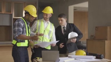 Architect discussing blueprints on laptop with construction manager Engineer talking to contractor consultant on construction site about construction project and business workflow in new building