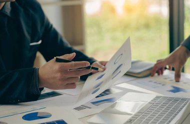 Businessman hand holding a pen pointing in document, financial graph, plan, marketing graph. Financial investment and business strategy data chart report and working on laptop in office