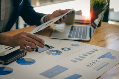 Businessman hand holding a pen pointing in document, financial graph, plan, marketing graph. Financial investment and business strategy data chart report and working on laptop in office