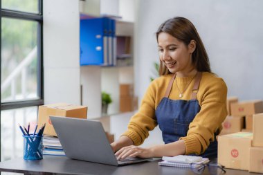 SME Online Business Ideas Small Business Startup A young Asian female entrepreneur uses a laptop computer to check online orders and prepare packages for customers.