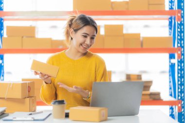 SME Online Business Ideas Small Business Startup A young Asian female entrepreneur uses a laptop computer to check online orders and prepare packages for customers.