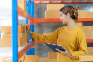 SME Online Business Ideas Small Business Startup A young Asian female entrepreneur uses a laptop computer to check online orders and prepare packages for customers.