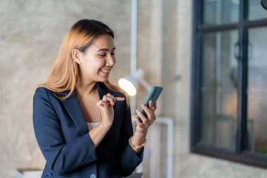 Asian female worker sitting in remote office holding smartphone using business applications or mobile work tools. Female freelancer checking email on mobile phone