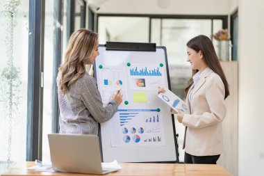 Two asian businesswoman standing discussing documents and discussing business plan strategy in office.