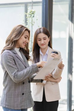 Two asian businesswoman standing discussing documents and discussing business plan strategy in office.