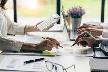 Profesyonel iş ortaklarından oluşan bir ekip elinde kalem tutarak mali grafik belgesini işaret ediyor, analiz ve strateji danışmanlığını hesaplıyor. Toplantı, ofiste beyin fırtınası, takım çalışması konsepti..