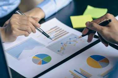 Profesyonel iş ortaklarından oluşan bir ekip elinde kalem tutarak mali grafik belgesini işaret ediyor, analiz ve strateji danışmanlığını hesaplıyor. Toplantı, ofiste beyin fırtınası, takım çalışması konsepti..